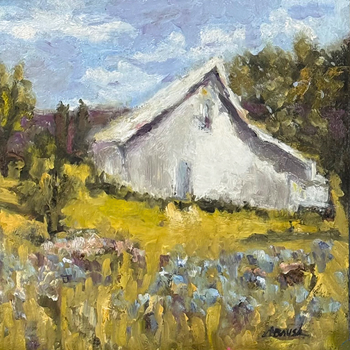 Colorful flowers grow in front of a pale barn on a bright and sunny day.
